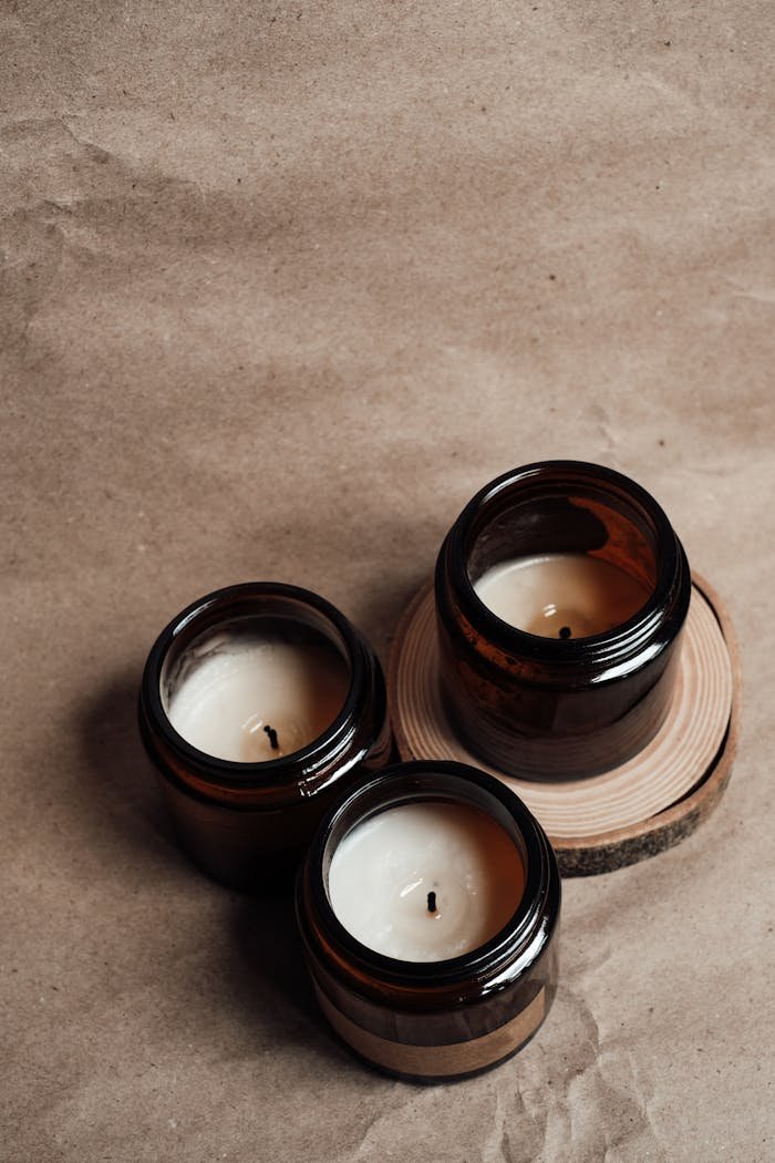 Why You Should Ditch Synthetic Scents and Switch to Essential Oils Three scented candles in amber glass jars arranged on a wooden slice, creating a cozy atmosphere.